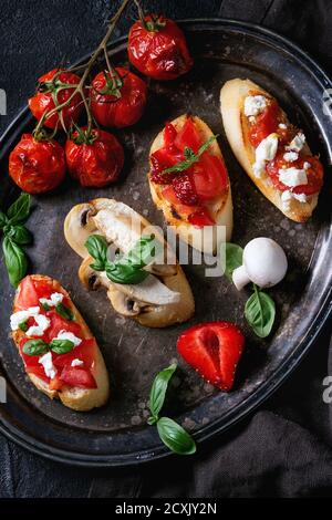 Verschiedene Mini-Bruschetta mit Tomaten, Erdbeeren, Feta-Käse, Huhn, Pilze und Basilikum auf getoastetem Baguette, serviert auf vintage Eisen Tablett Ove Stockfoto