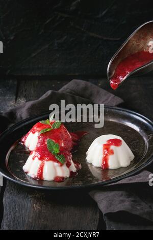 Hausgemachte Panna Cotta mit Erdbeersoße und frischer Minze, serviert auf vintage Eisen Tablett mit grauen Textil Serviette über alten Holzhintergrund. D Stockfoto