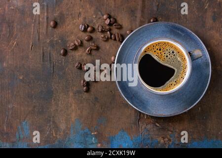Blaue Keramik Tasse schwarzen heißen Kaffee auf Untertasse, serviert mit Kaffeebohnen über alten Holz strukturierten Hintergrund. Draufsicht. Speicherplatz kopieren Stockfoto
