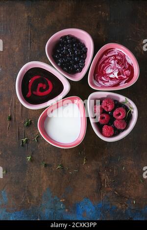 Fünf rosa Keramik Schalen von Beeren Dessert Suppen, Sahne und frische Heidelbeere und Himbeere, serviert über alten Holz strukturierten Hintergrund. Sommer gesund eati Stockfoto