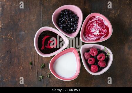 Fünf rosa Keramik Schalen von Beeren Dessert Suppen, Sahne und frische Heidelbeere und Himbeere, serviert über alten Holz strukturierten Hintergrund. Sommer gesund eati Stockfoto