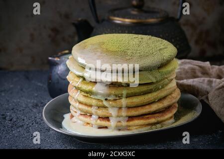 Stapel von hausgemachten amerikanischen Ombre grünen Tee Matcha Pfannkuchen mit Kondensmilchsauce und Matcha-Pulver auf grauem Teller serviert Mit Krug Sahne und teap Stockfoto