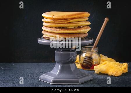 Stapel von hausgemachten amerikanischen Ombre gelb Kurkuma Pfannkuchen serviert auf Kuchenständer mit Glas Honig und Holzdipper über Schwarzer Stein Textur Hintergrund Stockfoto