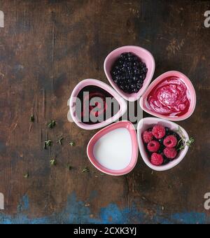 Fünf rosa Keramik Schalen von Beeren Dessert Suppen, Sahne und frische Heidelbeere und Himbeere, serviert über alten Holz strukturierten Hintergrund. Sommer gesund eati Stockfoto