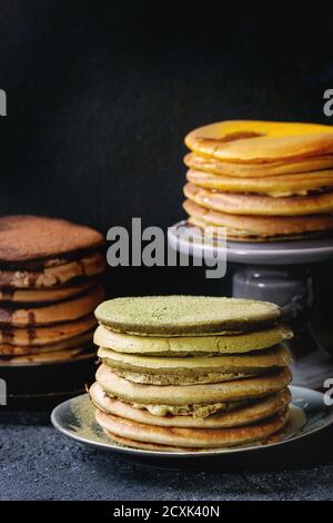 Auswahl an hausgemachten amerikanischen Ombre Schokolade, Grüntee Matcha und Kurkuma Pfannkuchen mit Honig und Sauce serviert auf Platten und Kuchen über schwarz s stehen Stockfoto