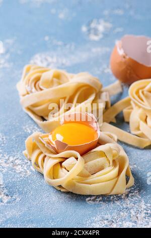 Frisches rohes hausgemachte verdrehten Teigwaren Tagliatelle mit Eigelb, Schale und Pasta Eierschneider über konkrete hellblauen Hintergrund. Stockfoto