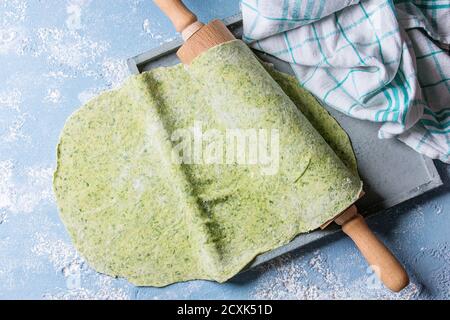 Frisch hausgemachter grüner Spinat gerollter Teig für Pasta Tagliatelle auf Holz-Nudelholz mit Küchentuch über hellblauem Beton Hintergrund. Draufsicht Stockfoto