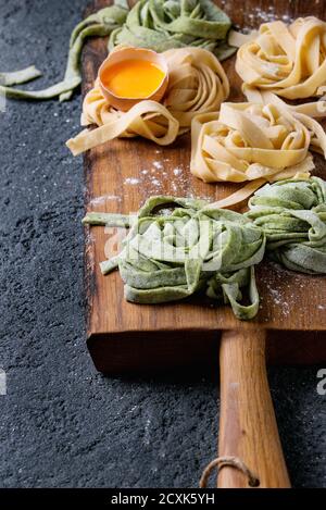 Verschiedene farbige frische rohe hausgemachte Teigwaren Tagliatelle grün Spinat und traditionellen gelb mit Eigelb auf Holzbrett über dunkel Stockfoto