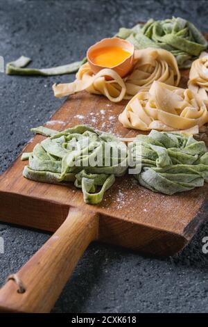 Verschiedene farbige frische rohe hausgemachte Teigwaren Tagliatelle grün Spinat und traditionellen gelb mit Eigelb auf Holzbrett über dunkel Stockfoto