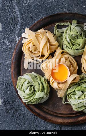 Verschiedene farbige frische rohe hausgemachte Teigwaren Tagliatelle grün Spinat und traditionellen gelb mit Eigelb auf Holzbrett über dunkel Stockfoto