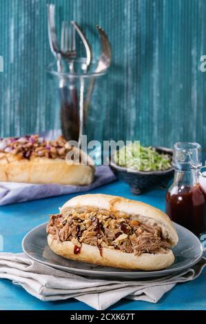 Auswahl an Pulled Pork Sandwiches mit Fleisch, gebratenen Zwiebeln, grünen Sprossen und bbq Ketchup, serviert auf grauem Teller und Textil mit einer kleinen Flasche Tomaten Stockfoto