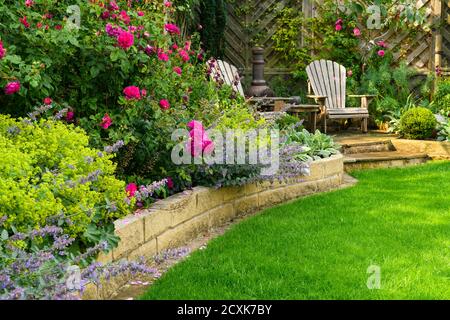 Landschaftlich schöner, sonniger privater Garten (modernes Design, farbenfrohe Sommerblumen, Randpflanzen, Sitzmöbel auf der Terrasse, Rasen) - Yorkshire, England, Großbritannien Stockfoto