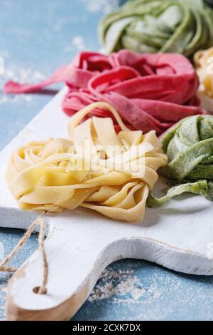 Verschiedene farbige frische rohe hausgemachte Teigwaren Tagliatelle grün Spinat, rosa rote Beete und traditionellen gelb auf weißem Holz schneiden Board ove Stockfoto