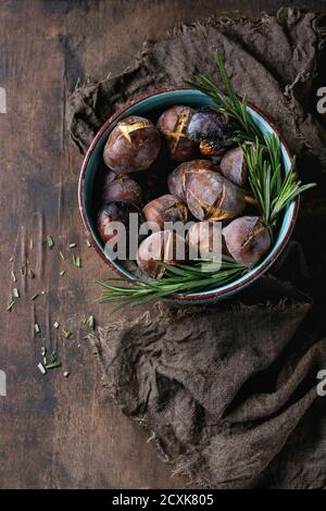 Gebratene Kastanien in der Asche mit Rosmarin in Türkis Keramikschale auf Sackleinen über alten dunklen hölzernen Hintergrund. Draufsicht mit Platz für Text. Stockfoto