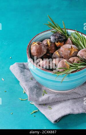 Gebratene Kastanien in der Asche mit Rosmarin in Türkis Keramikschale auf Textile Serviette über hellen blauen hölzernen Hintergrund. Stockfoto