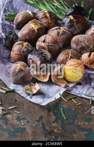 Geröstete Kastanien in der Asche mit Rosmarin auf Papier über alten dunklen Textur Holzhintergrund. Nahaufnahme mit Platz für Text. Stockfoto