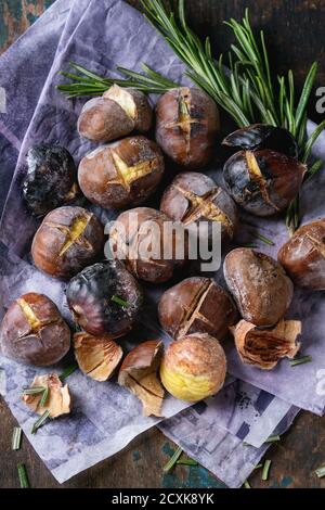 Geröstete Kastanien in der Asche mit Rosmarin auf Papier über alten dunklen Textur Holzhintergrund. Nahaufnahme. Stockfoto