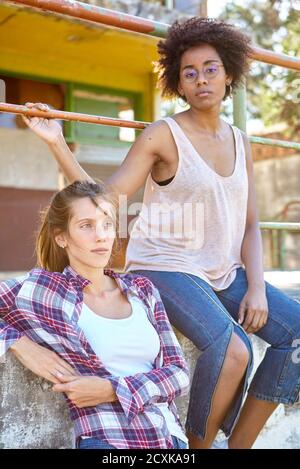 Junge Frauen blicken weg, während sie an der Wand sitzen Stockfoto