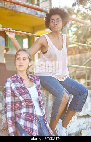 Junge Frauen blicken weg, während sie an der Wand sitzen Stockfoto