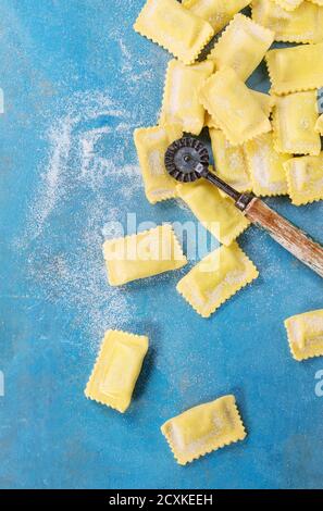 Frisch markiert rohe italienische Teigwaren-Ravioli mit Mehl und Vintage Nudeln Cutter über hellen blauen hölzernen Hintergrund. Draufsicht mit Textfreiraum. Stockfoto