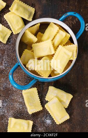 Frisch zubereitete rohe, ungekochte italienische Pasta Ravioli in vintage blauer Pfanne auf altem dunklen Holzhintergrund. Draufsicht, Nahaufnahme Stockfoto