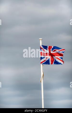 Union Jack Flagge fliegen in starkem Wind auf bewölktem Hintergrund Stockfoto