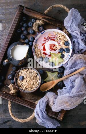Smoothie Schüssel gesundes Frühstück. Erdbeer-Joghurt mit Müsli, Minze, Heidelbeeren, Krug mit Milch und Karambole in Holztablett auf Textile Gaze über dar Stockfoto