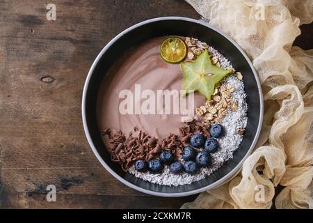 Smoothie Schüssel gesundes Frühstück. Schokolade Joghurt mit Heidelbeeren, Müsli, Kokos, Limette und Karambole auf Textile Gaze über dunklem Holz Textur bac Stockfoto