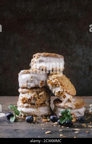 Set mit hausgemachtem Eis Sandwiches in oat Cookies mit Mandel Zucker Krümel, Blaubeeren und Minze über Dark Metal Textur Hintergrund. Nahaufnahme Stockfoto