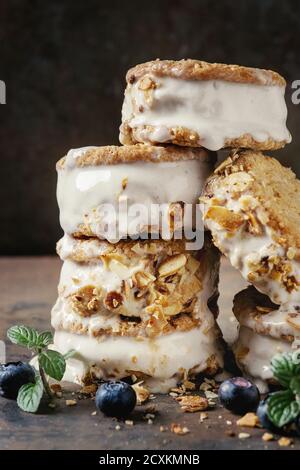 Set mit hausgemachtem Eis Sandwiches in oat Cookies mit Mandel Zucker Krümel, Blaubeeren und Minze über Dark Metal Textur Hintergrund. Nahaufnahme Stockfoto