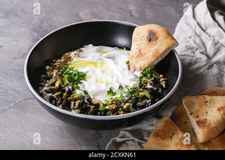 Labneh im Nahen und Mittleren Osten libanesischen Cream Cheese Dip mit Olivenöl, Salz, Kräuter, Oliven Tapenade in schwarz Schüssel mit traditionellen pita Brot über gra serviert. Stockfoto