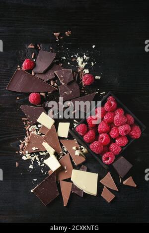 Vielzahl von dunklen, verbrannt Milch und weiße Schokolade mit frischen Himbeeren in schwarzer Holzbox über schwarz hacken Holz Hintergrund. Ansicht von oben mit dem Raum. C Stockfoto