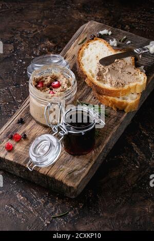 Gläsern Huhn Leber Pastete mit schwarzer Johannisbeere Marmelade, Granatapfel Korn und Schnittbrot, serviert mit Vintage Messer auf Schneidbrett aus Holz über da Stockfoto