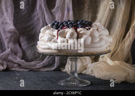 Hausgemachtes Baiser Kuchen Pavlova mit Schlagsahne, frische Heidelbeeren und Blaubeerensauce auf Vintage Etagere auf schwarzen Betontextur Hintergrund, g Stockfoto