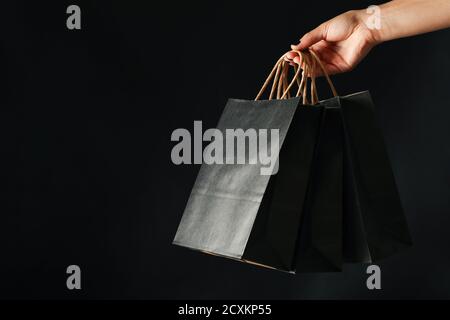 Hand mit Papiertüten auf einem schwarzen Hintergrund, Einkaufstüten in der Frauenhand für Black Friday und Einzelhandelsförderung Stockfoto