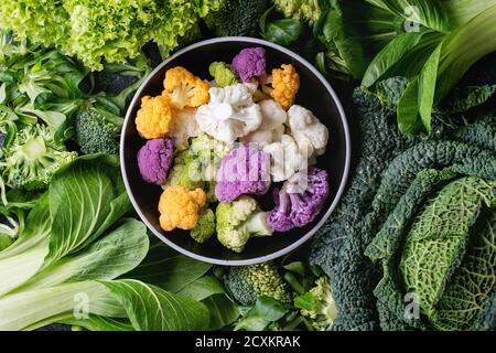 Vielzahl von rohem Gemüse Salate, Salat, Chinakohl, Mais, Brokkoli, Wirsing runden bunten jungen Blumenkohl in schwarz Schüssel. Essen staatlich Stockfoto