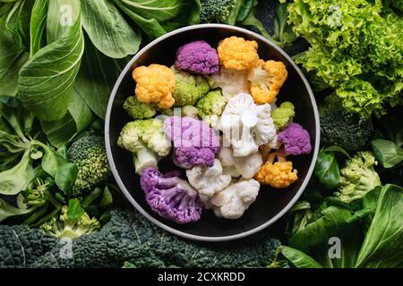 Vielzahl von rohem Gemüse Salate, Salat, Chinakohl, Mais, Brokkoli, Wirsing runden bunten jungen Blumenkohl in schwarz Schüssel. Essen staatlich Stockfoto