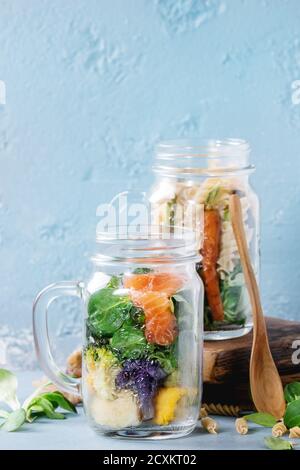 Vielzahl von Gemüsesalaten in Einweckgläser. Salat mit grünen, Nudeln, Karotten, Blumenkohl, Lachs. B überragt mit Holzlöffel und servieren board Stockfoto