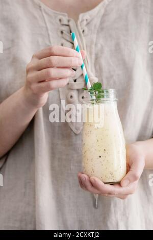 Eine Flasche Smoothie mit Chia-Samen, Heidelbeeren, Minze und retro gestreiftes cocktail Rohr in weiblichen Händen. Frau in weißem Leinen Kleid. Gesunde eati Stockfoto