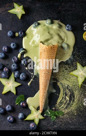 Waffel Kegel von Schmelzen Grüner Tee matcha Weich-elastische Eis mit Minze, Karambolen, Kalk, Blaubeeren über schwarzen Textur Hintergrund. Ansicht von oben. Stockfoto