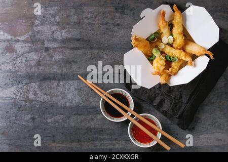 Fried-Tempura-Garnelen mit Reis und Frühlingszwiebeln in Pappschachtel zum mitnehmen. Serviert mit Saucen, Stäbchen über alte Metall Hintergrund. Ansicht von oben, Raum. Asiatische Stockfoto