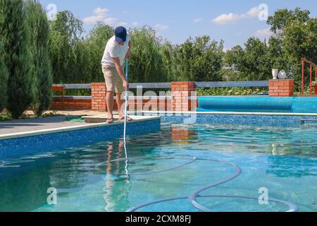 Der Pool war sauberer. Mann, der im Sommer den Außenpool mit Staubsauger reinigt. Saisonale Zubereitungen. Reinigungssysteme zum Schwimmen Stockfoto