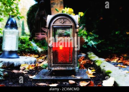 Alte Grablaterne mit brennender Kerze in der Dämmerung auf einem Friedhof im Herbst Stockfoto