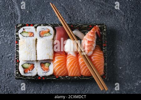 Sushi Nigiri und Sushi Rolls Set in Kunststoff-Lebensmittel Lieferbox mit Stäbchen über schwarzen Stein Textur Hintergrund. Ansicht von oben mit dem Raum. Japan-Menü Stockfoto