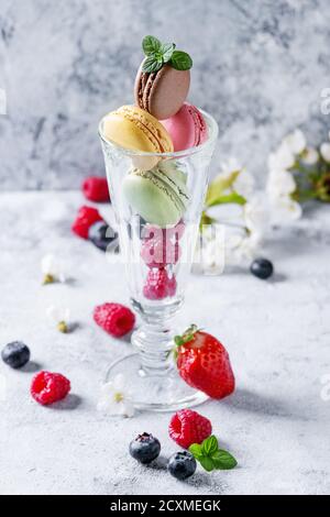 Vielfalt von bunten französischen süße Nachspeise macaron Makronen mit verschiedenen Füllungen aus Glas mit Frühling Blumen und frischen Beeren über graues Tex serviert. Stockfoto