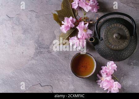 Schwarzes Eisen-Teekanne und traditionelle Keramik Tasse Tee mit Blüte rosa Blumen Kirsche Zweig über graue Textur Hintergrund. Draufsicht mit Raum, asiatisch Stockfoto