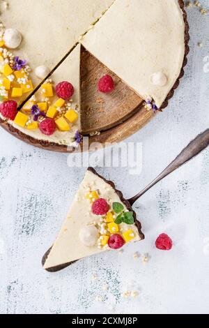 Hausgemachte geschnittene Schokolade Tarte von Mango, Himbeeren, Minze dekoriert, aufgeblasen Reis und essbare Blüten mit Stück Torte auf Kuchen Schaufel über den weißen text Stockfoto