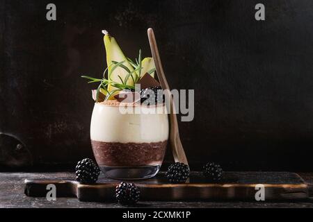 Dessert Frühstück geschichteten Chia-Samen, Schoko-Pudding, Reis Brei aus Glas dekoriert mit frischen Brombeeren, Birne, Kakaopulver. Stehen mit Löffel Stockfoto