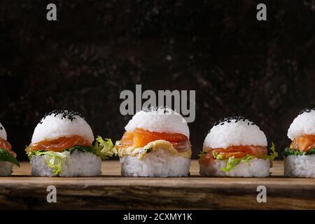 Mini Reis sushi Burger mit geräuchertem Lachs, grüner Salat und Saucen, schwarzer Sesam mit Stäbchen aus Holz Über Holz Hintergrund serviert. Moderne gesunde fo Stockfoto