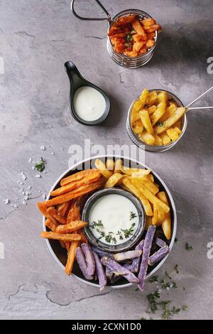Auswahl an pommes Frites traditionelle Kartoffeln, lila Kartoffel, Karotte mit Weißkäse-Sauce, Salz, Thymian in schwarzer Schüssel über graue Textur backgr serviert Stockfoto